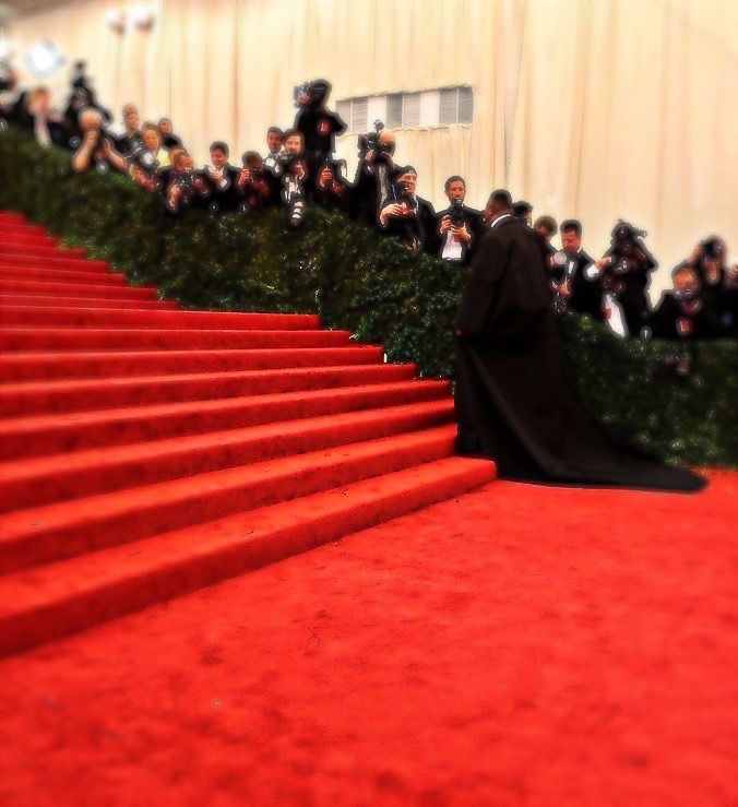 a woman in a black gown is walking down the red carpeted stairs with cameras around her