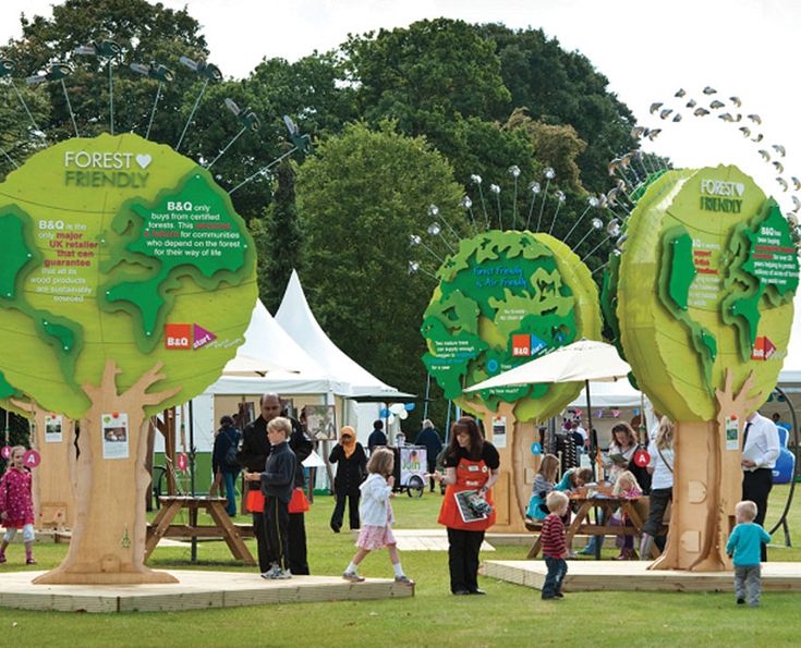 people are standing in front of trees with green leaves on them at an outdoor event