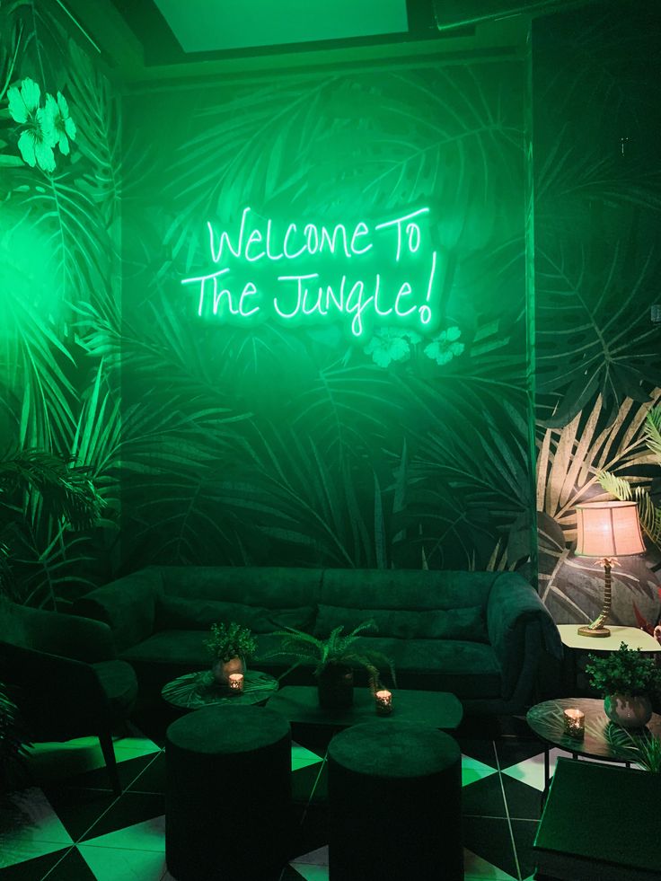 a green neon sign that reads welcome to the jungle in front of a black and white checkered floor