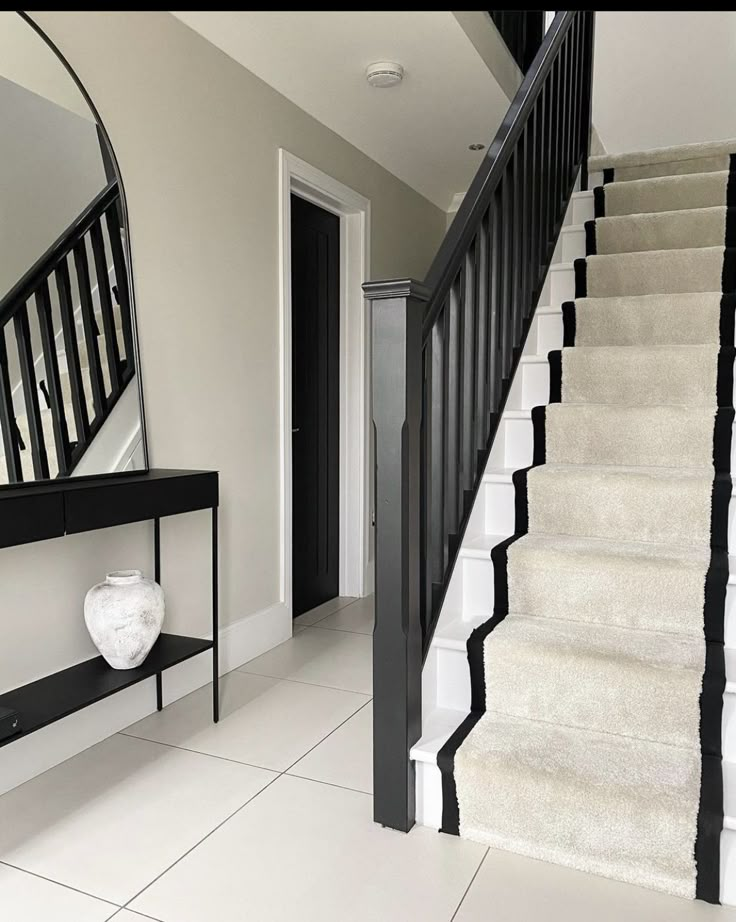 a black and white staircase with a mirror on the wall next to an entryway