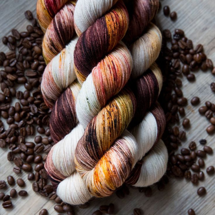 several skeins of yarn sitting next to coffee beans on a wooden surface with brown and white speckles