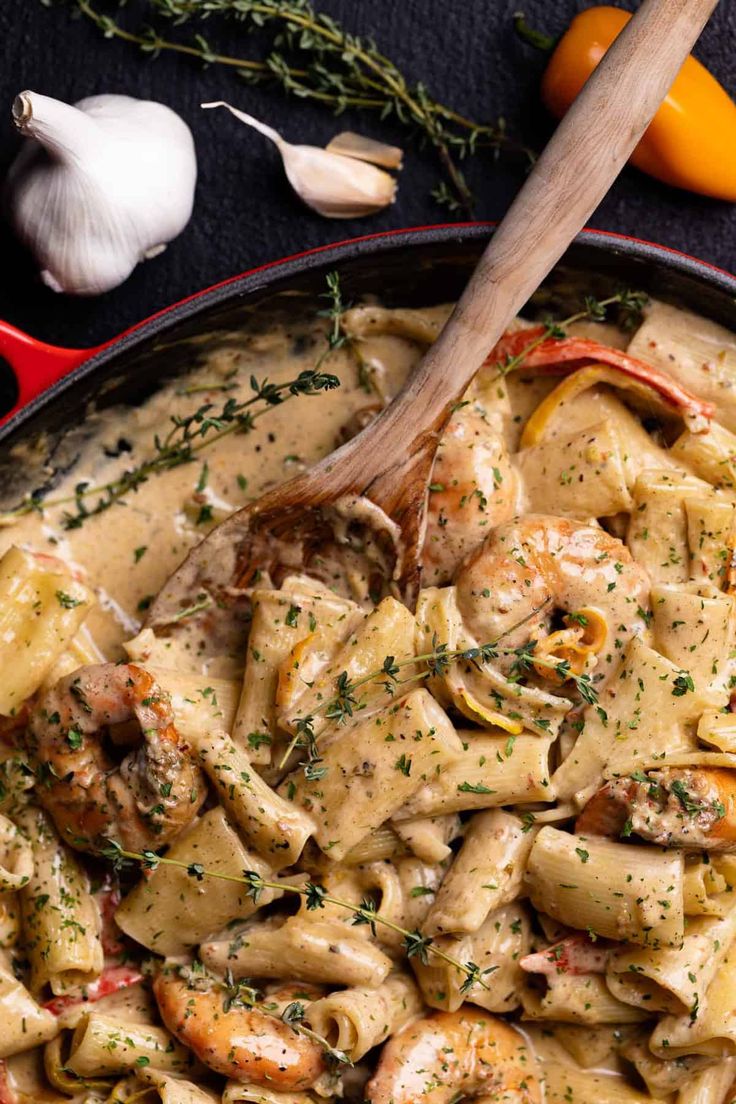 a skillet filled with pasta and shrimp next to garlic, peppers, and an orange