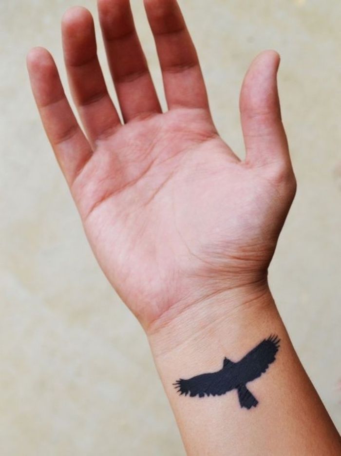 a person's hand with a small black bird tattoo on the wrist and arm