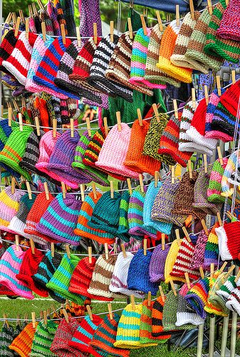 colorful knitted hats and sweaters hanging on clothes pins in the grass at an outdoor market