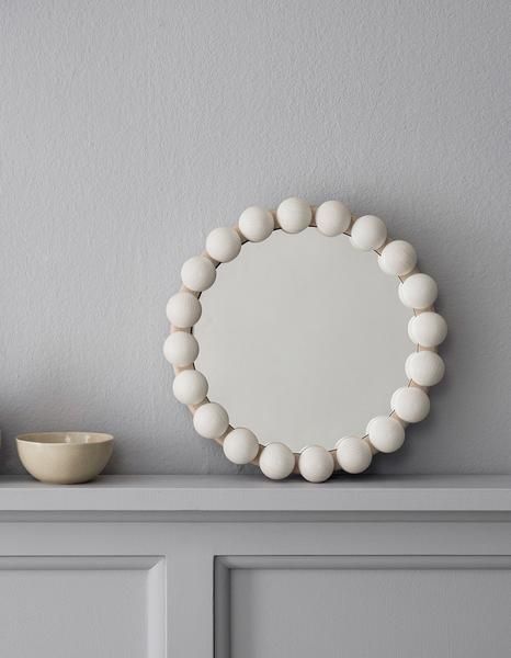 a round mirror sitting on top of a white shelf next to a bowl and cup