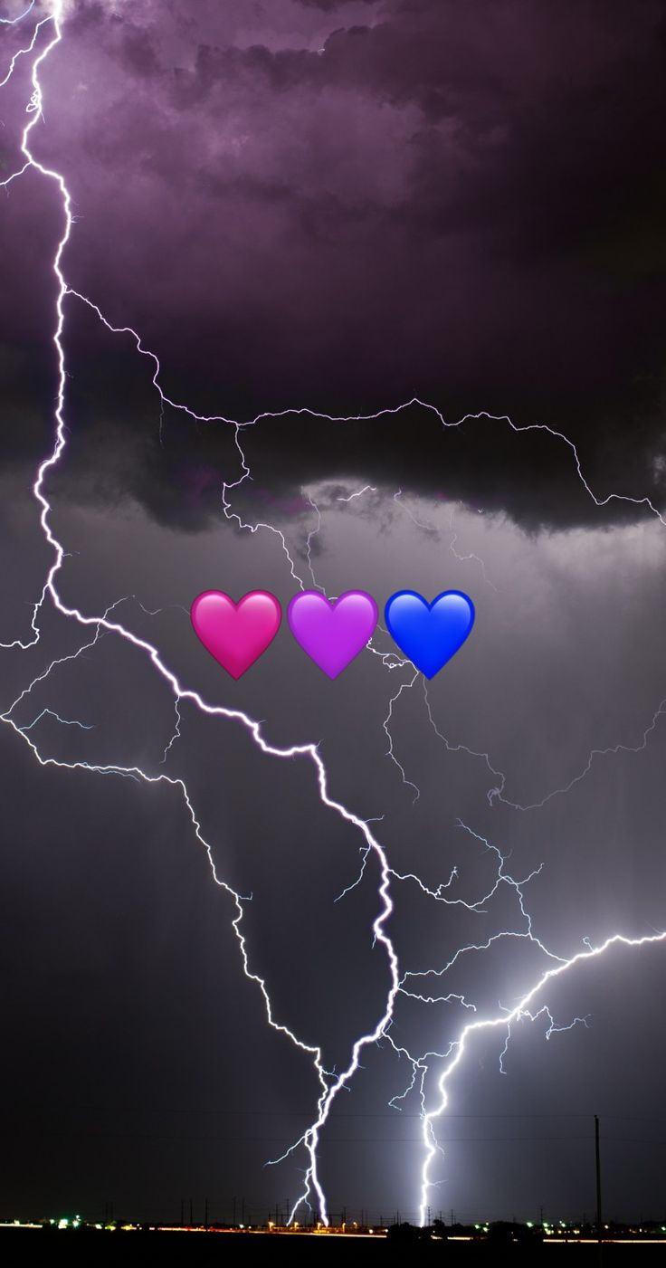 three heart shaped balloons floating in the air with lightning behind them on a cloudy night