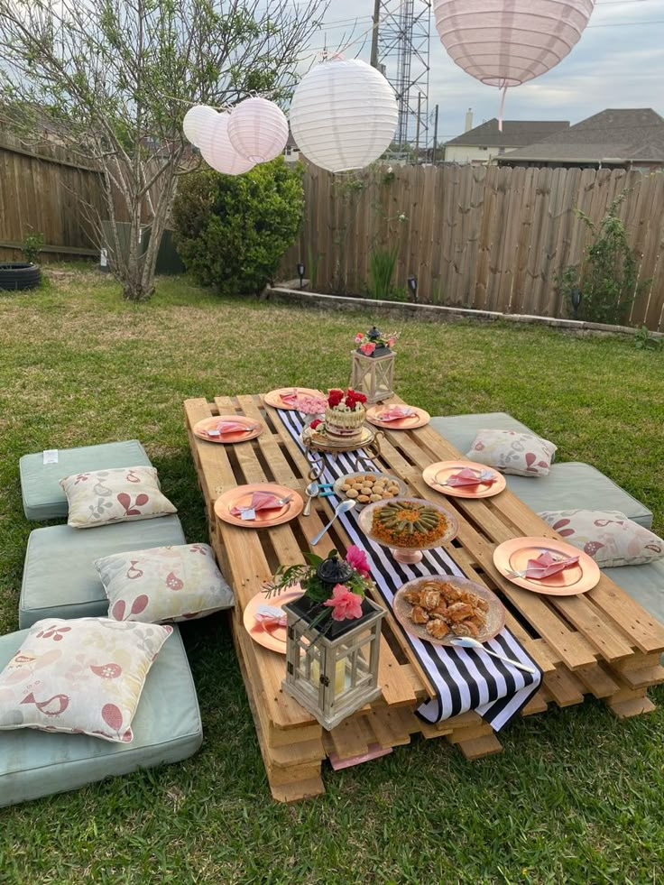 a picnic table set up in the back yard with plates and food on it,