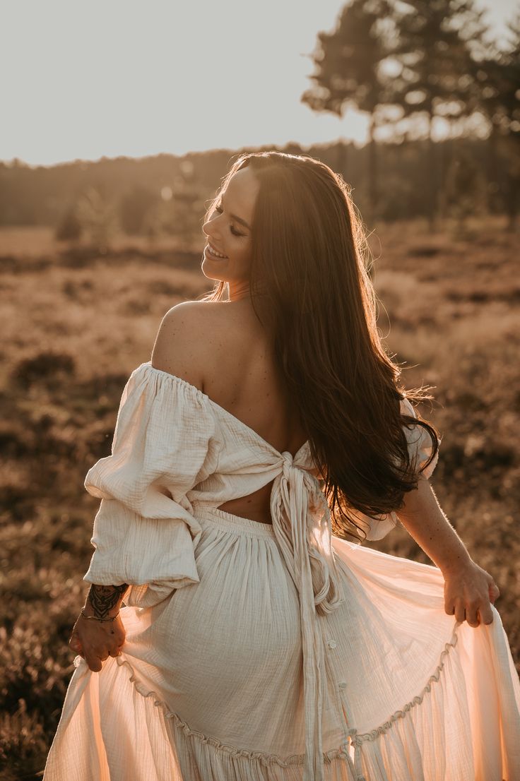 a woman standing in a field with her back to the camera, wearing a white dress