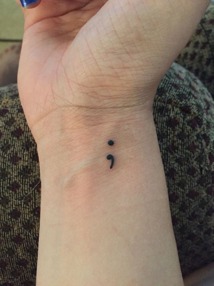 a woman's wrist with a small black dot tattoo on the left side of her arm