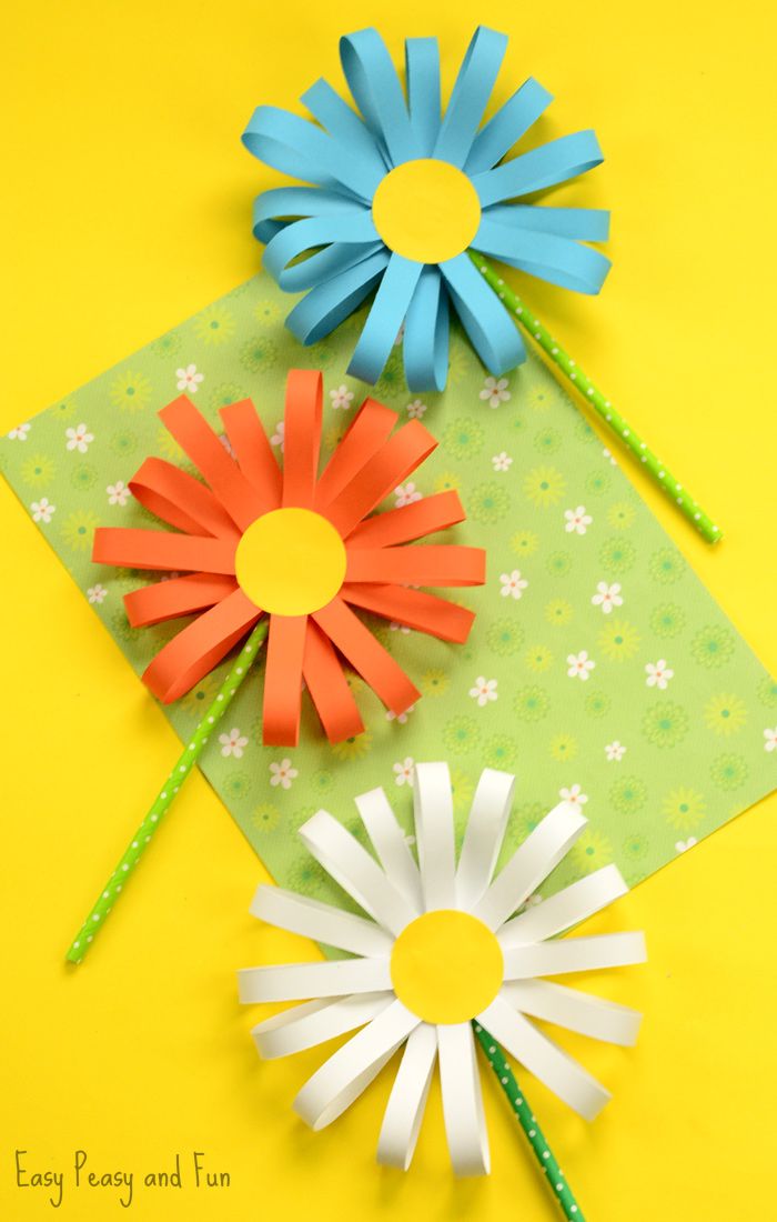 three paper flowers sitting on top of a green and yellow surface with pencils in the middle