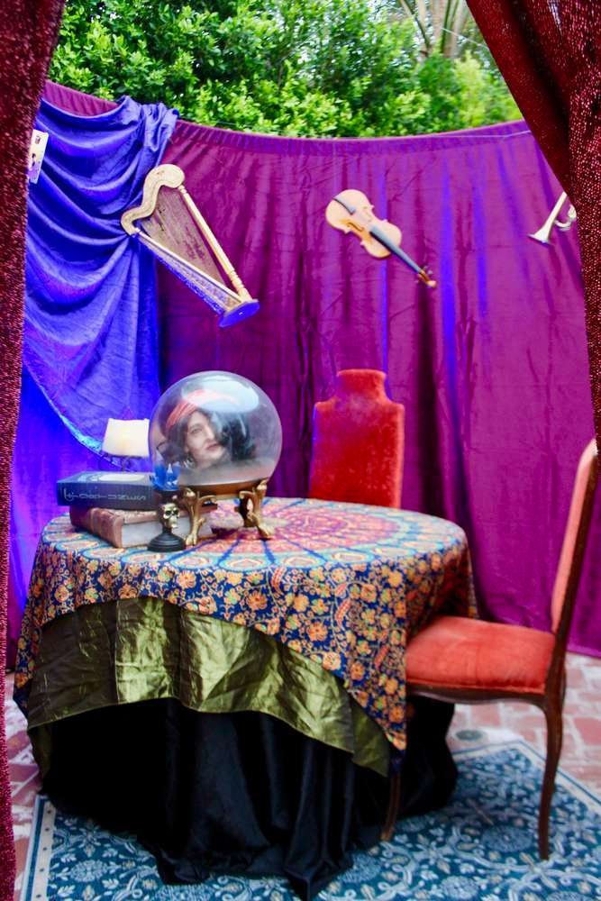 the table is covered with purple cloth and has a glass dome on it, surrounded by red velvet drapes