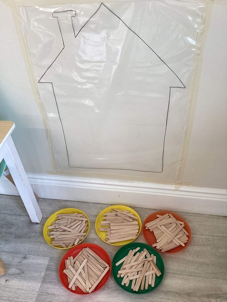 four plates with popsicle sticks in front of a house cutout on the wall