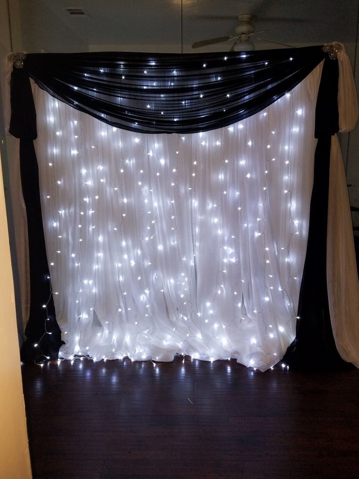 a white curtain with lights on it in front of a wall that is decorated with black and white drapes