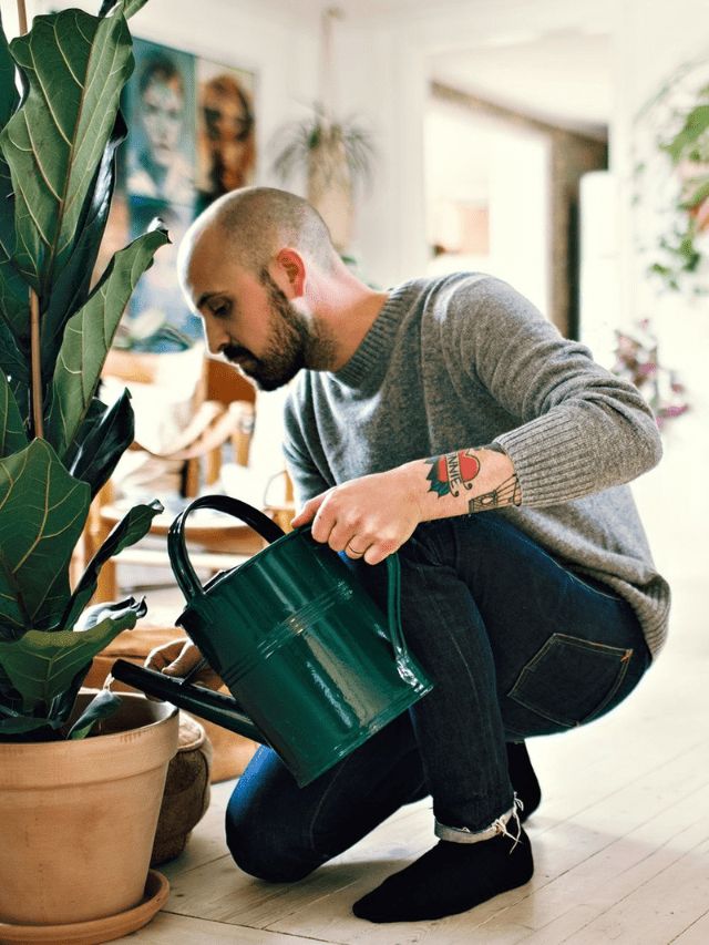 a man kneeling down next to a potted plant and holding a green watering can