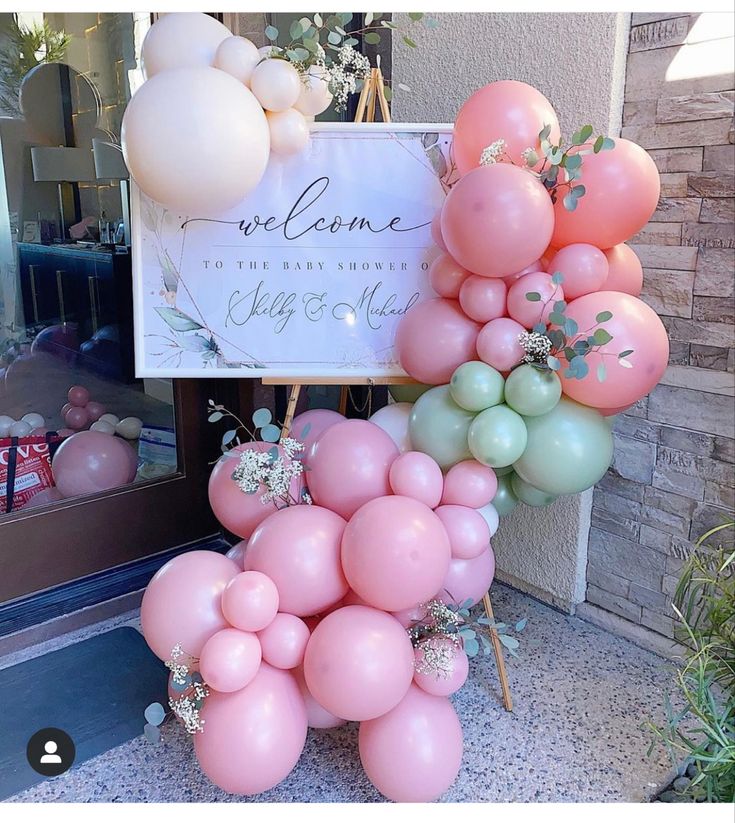 a welcome sign made out of balloons and greenery in front of a storefront