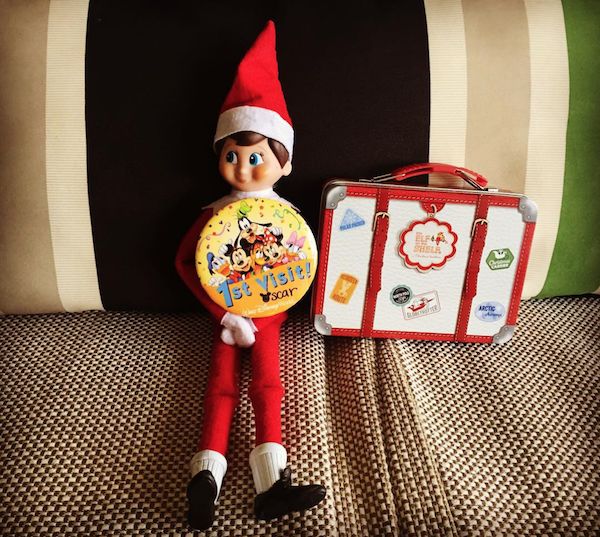 an elf is holding a pizza plate next to a suitcase on a bed with a striped pillow