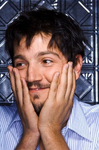 a man smiling with his hands on his face and looking at the camera while wearing a blue striped shirt