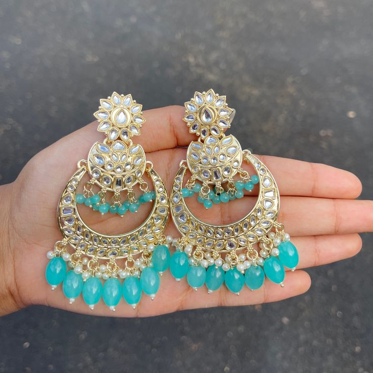 The Teal Sayana Earrings are lightweight chandbalis with Kundan and Gold-Plating on beautiful beaded crystals. Specifications Materials used: Kundan, beaded crystals, Gold Plating Weight: 24 g Height: 3 inches At Romikas, we pride ourselves on the craftsmanship and high quality of our jewelry, designed to enhance your natural beauty. Please contact us with any questions. Beaded Chandelier Earrings For Weddings And Festivals, Wedding Chandelier Earrings With Beads, Chandbali Jewelry With Dangling Beads For Diwali, Bollywood Chandbali Jewelry With Dangling Beads, Bollywood Style Chandbali Jewelry With Dangling Beads, Kundan Chandbalis With Dangling Beads, Jeweled Chandbalis For Festivals, Festival Chandbali Bridal Earrings With Beads, Beaded Chandbali Earrings For Celebration