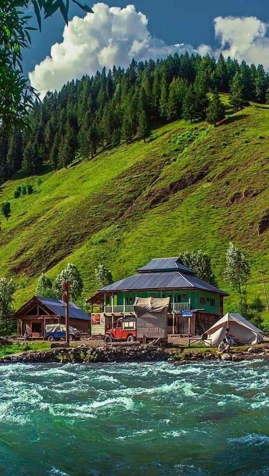 some houses are on the side of a hill by the water with green hills in the background