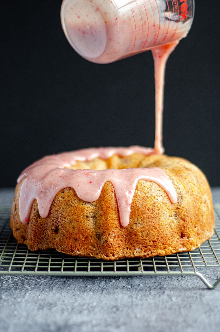 someone pouring icing onto a bundt cake on a cooling rack