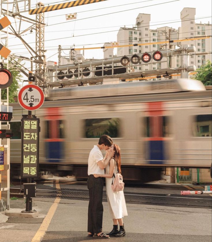 a man and woman standing on the side of a road next to a train track