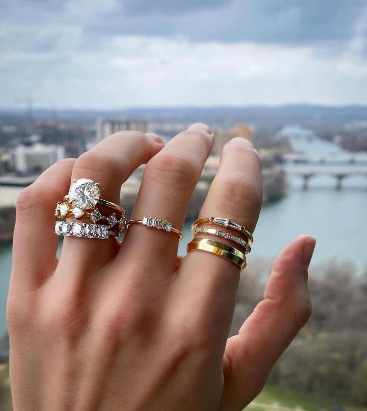 a woman's hand holding three different rings in front of her face, with the view of a river below