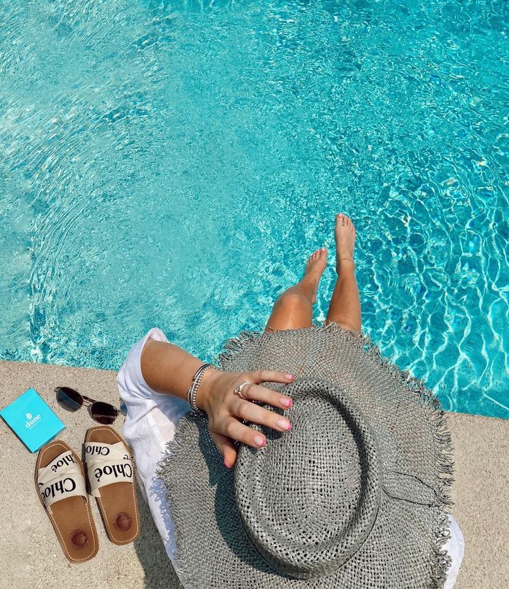 a woman laying next to a swimming pool with her feet up on the beach towel