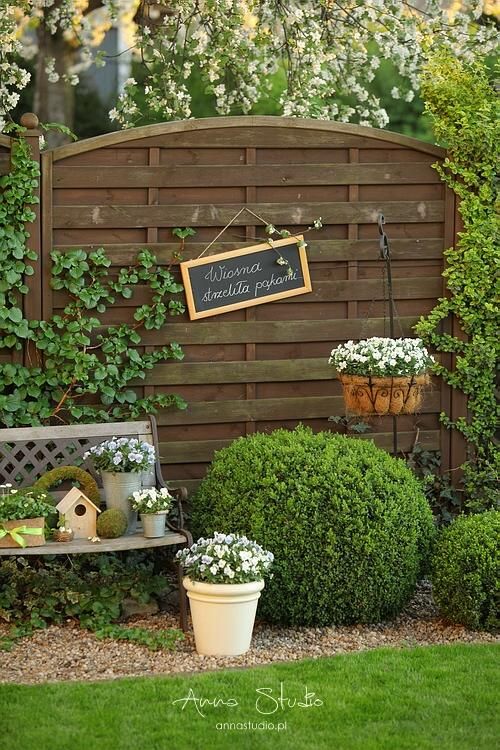 a wooden bench sitting in the middle of a lush green yard with white flowers and potted plants