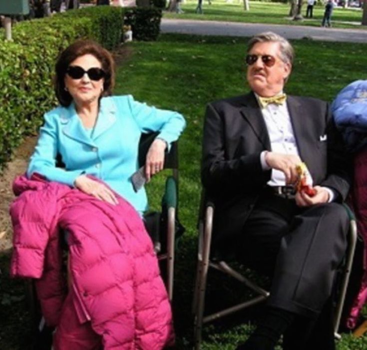 two people sitting on lawn chairs in the grass with one person wearing a suit and tie