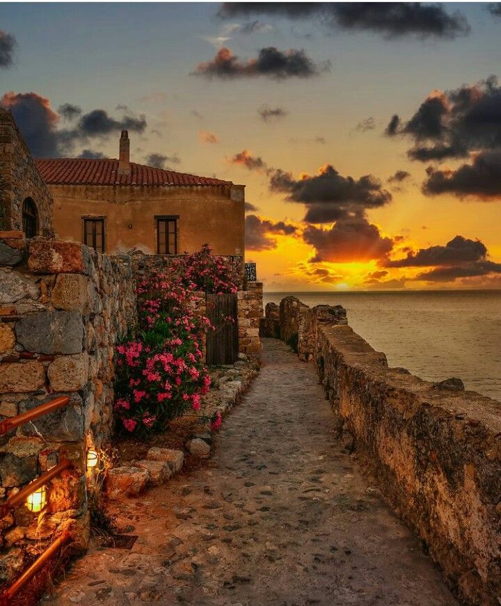 the sun is setting over an old stone building by the ocean with flowers growing on it