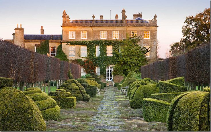 a large building with many hedges in front of it and a stone pathway leading to the entrance