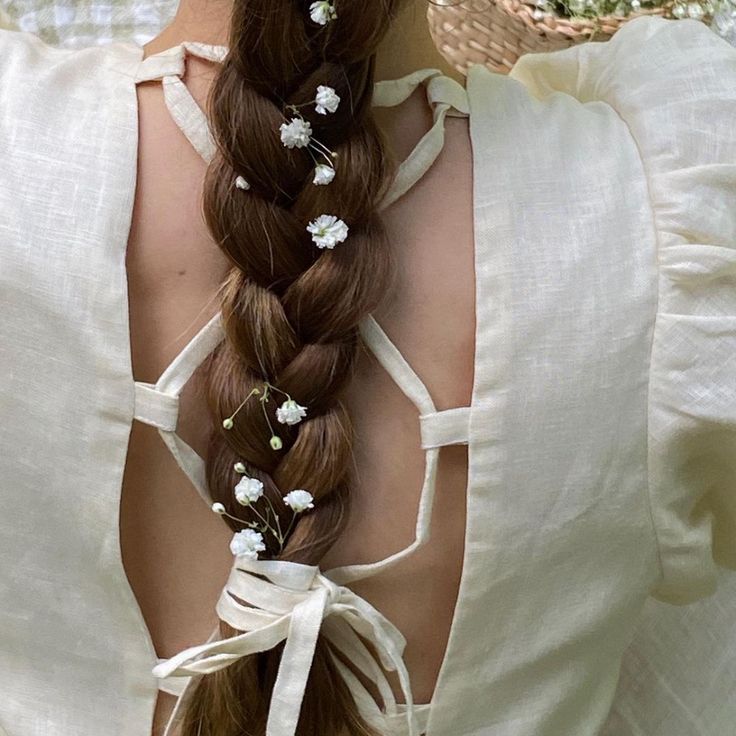 a woman with long brown hair wearing a white dress and flower crown braid in her hair