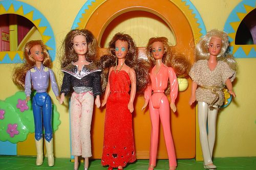 five barbie dolls are lined up in front of a play house with colorful walls and arches