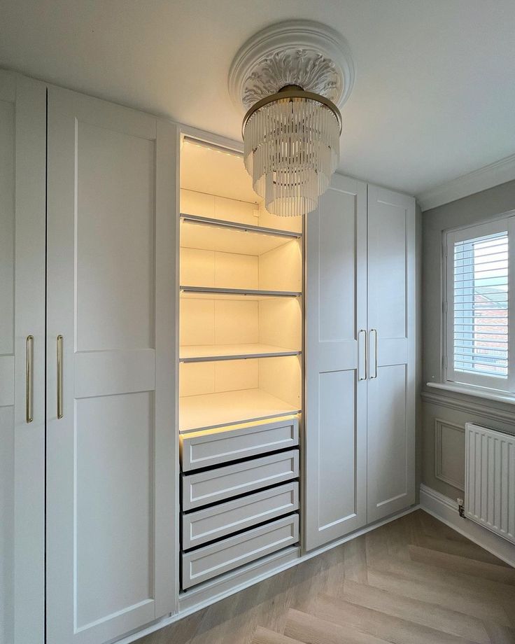 an empty room with white cupboards and lights on the ceiling is lit by a crystal chandelier