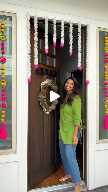 a woman standing in front of a door with decorations on the outside and pink tassels hanging from it