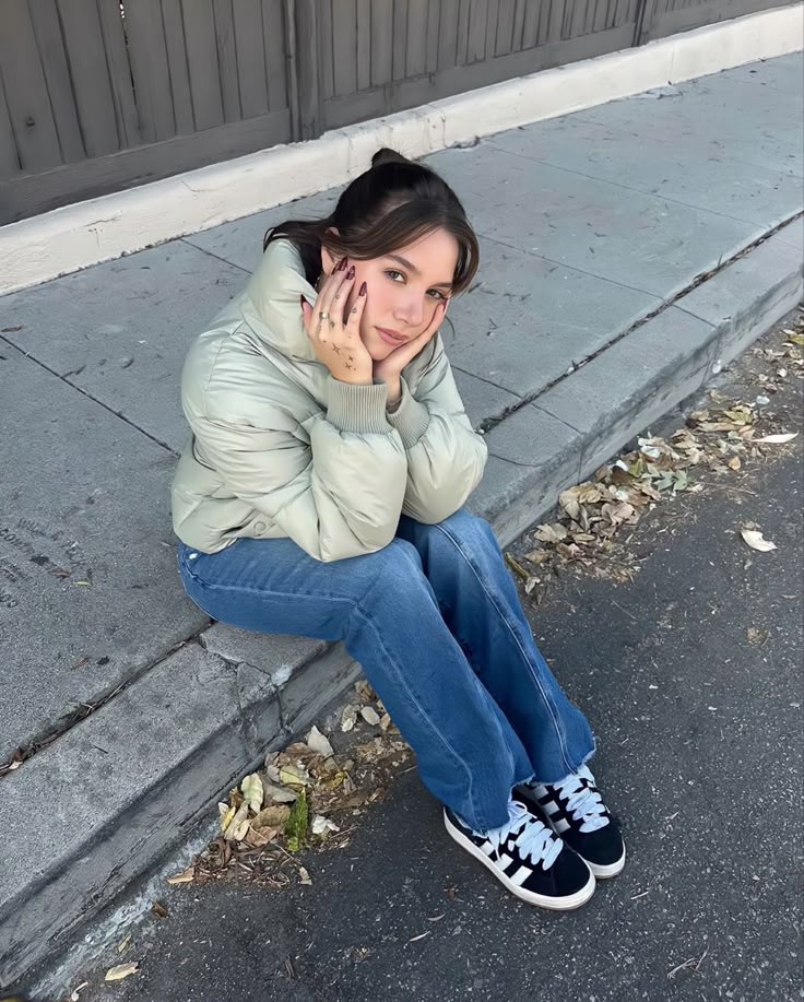 a woman is sitting on the curb talking on her cell phone and looking at the camera