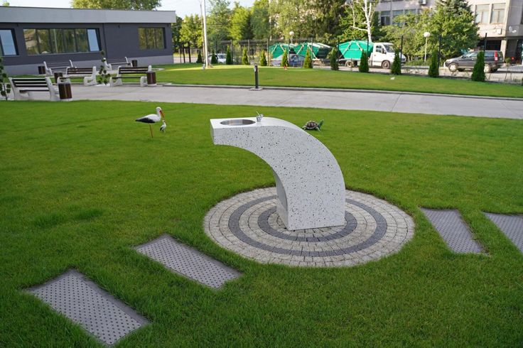 a sculpture in the middle of a grassy area with steps leading up to it and birds walking around