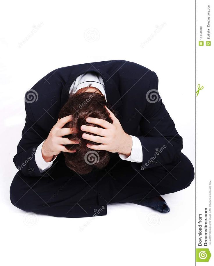 a man in a suit and tie covering his face with his hands while sitting on the floor