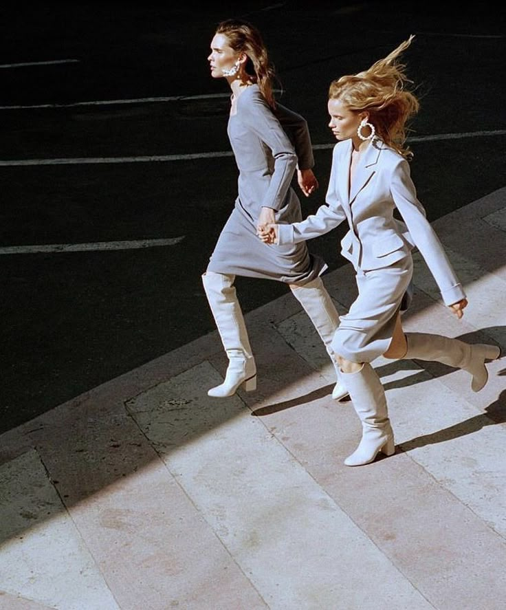 two women are walking down the street in white boots and jackets, one is holding her hand