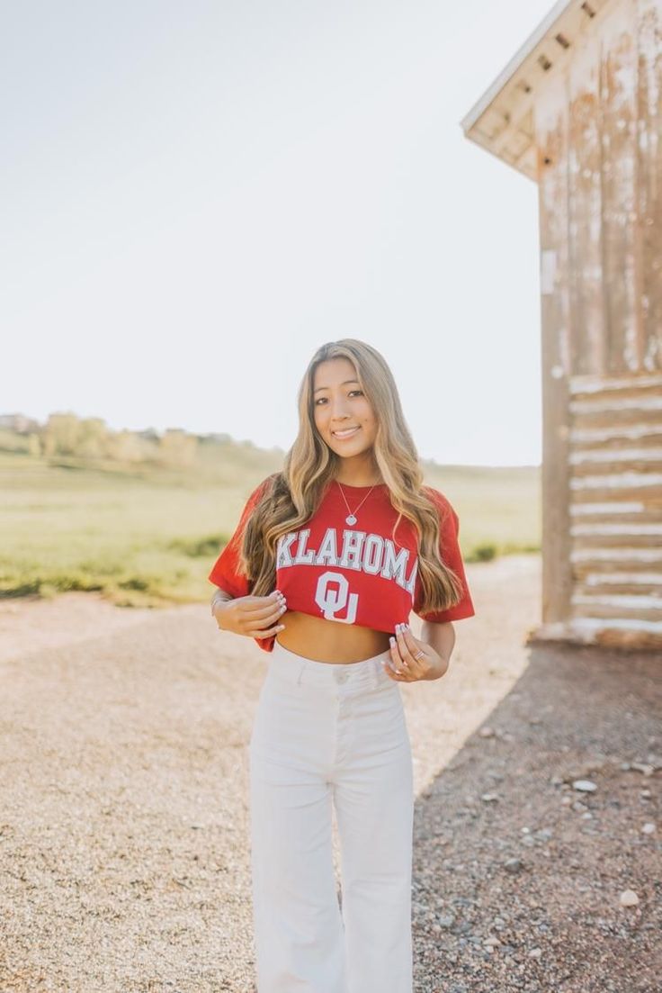 a woman standing in front of a barn wearing a red shirt and white pants with the word