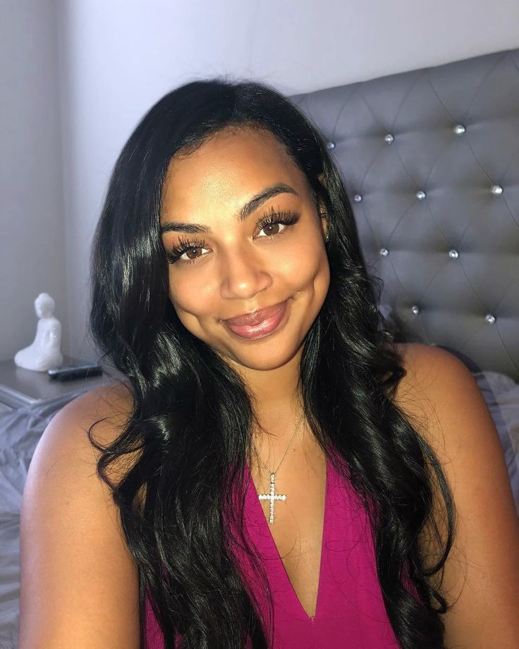 a woman in a pink dress sitting on a bed with a cross necklace around her neck