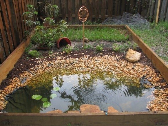 a small pond in the middle of a garden with rocks and gravel around it, surrounded by a wooden fence