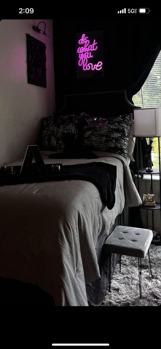 a bed room with a neatly made bed and a neon sign on the wall above it