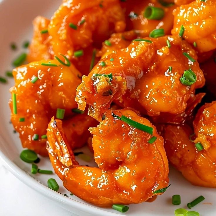 a white plate topped with fried shrimp and garnished with green onions on top