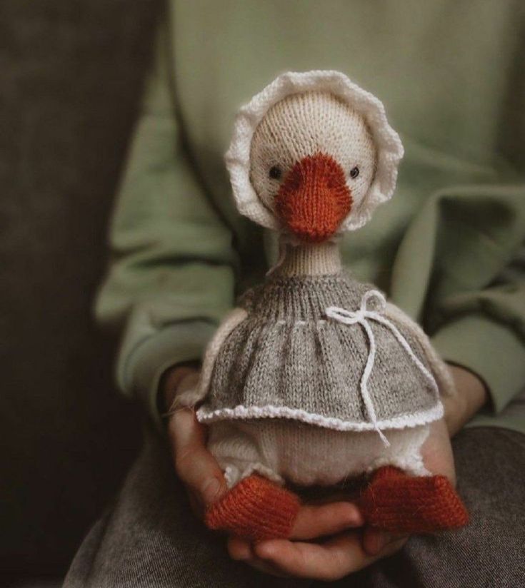 a person holding a knitted duck doll in their hands, wearing a dress and bonnet