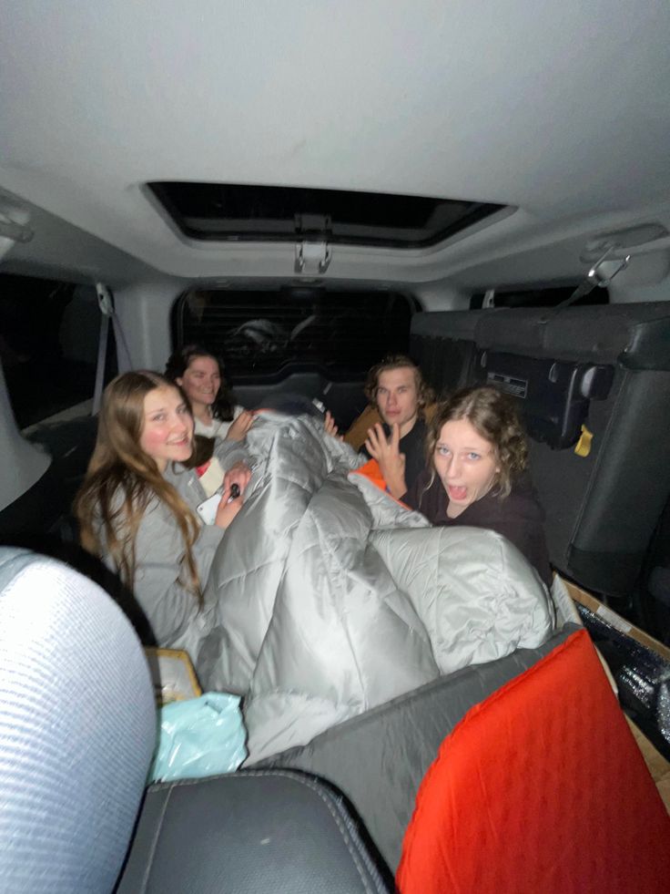 group of people sitting in the back of a van with blankets on it's sides