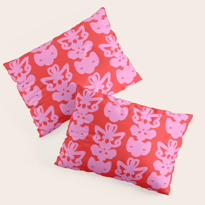 two red pillows with pink flowers and hearts on them, sitting side by side in front of a white background