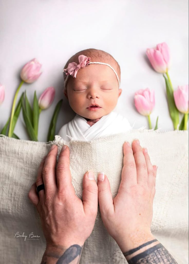 a baby is sleeping on top of someone's lap with pink tulips in the background