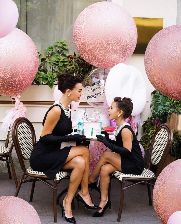 two women sitting at a table in front of balloons