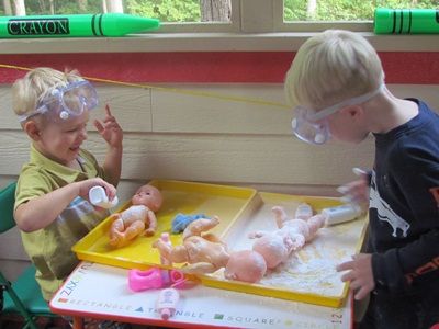 two young boys playing with toys in a playroom at the same time and wearing goggles